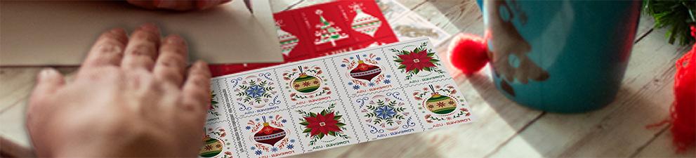 A person addressing a letter with First-Class Mail Forever® holiday stamps on the table.