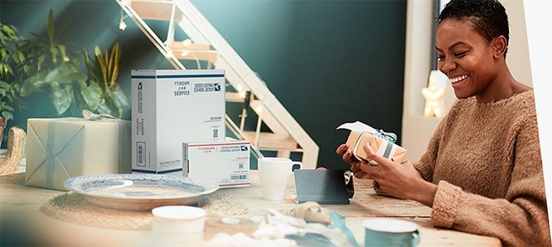 A woman on a laptop preparing to ship Priority Mail boxes and a card with a holiday-themed stamp.